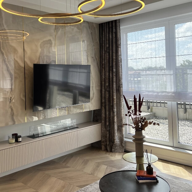 Nowoczesny salon z telewizorem na ścianie, okrągłymi lampami sufitowymi i dużym oknem z zasłoną.