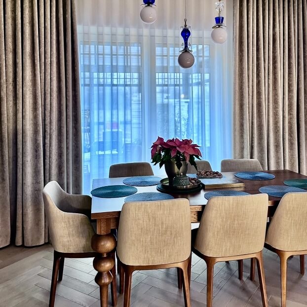 Jasna jadalnia z drewnianym stołem, krzesłami, dekoracją z poinsecji i niebieskimi lampami wiszącymi pod sufitem.