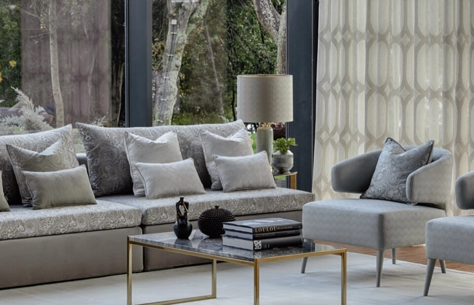 Elegancki salon z szarymi sofami, poduszkami i stolikiem kawowym. Duże okna z widokiem na ogród.