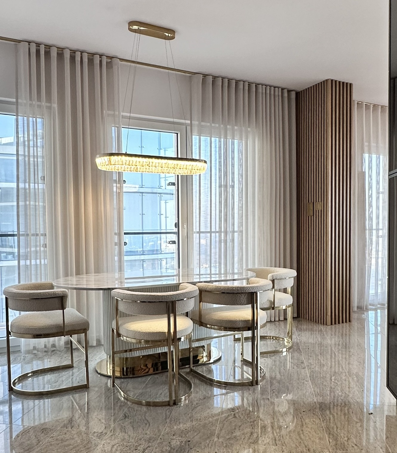 Elegancki salon z marmurową podłogą, stołem i krzesłami. Duże okna z zasłonami, a nad stołem wisząca lampa.