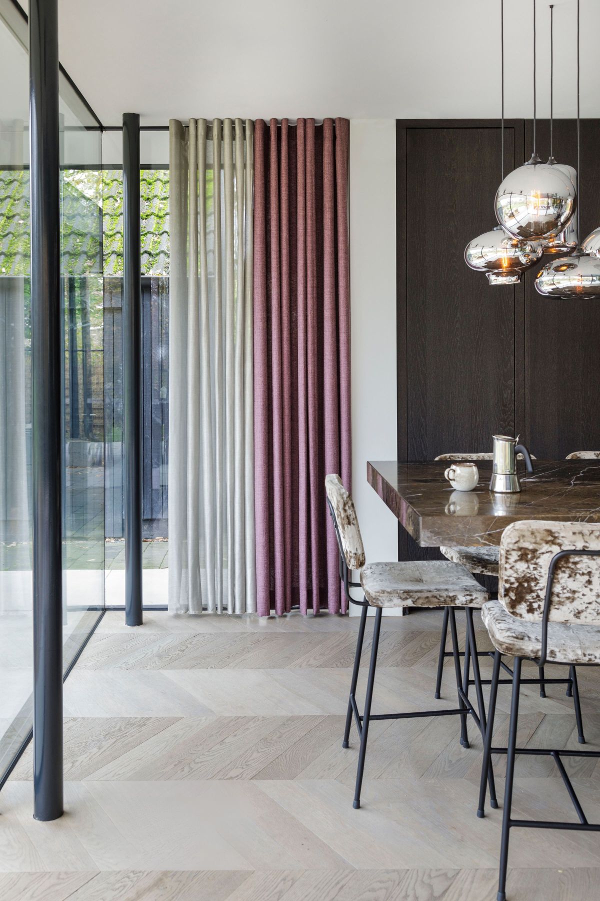 Nowoczesne wnętrze z dużymi oknami, eleganckimi zasłonami i designerskimi krzesłami przy stole jadalnym.