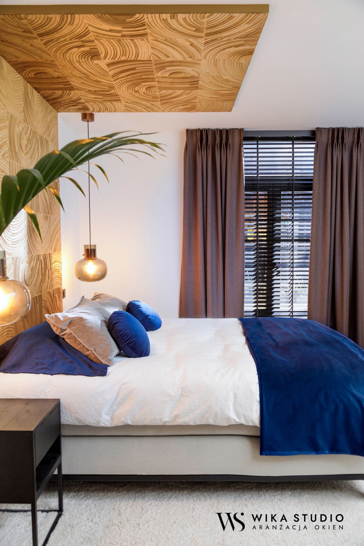 Sypialnia z niebieskimi akcentami, drewnianym sufitem i nowoczesnym oświetleniem, zasłony przy oknie.