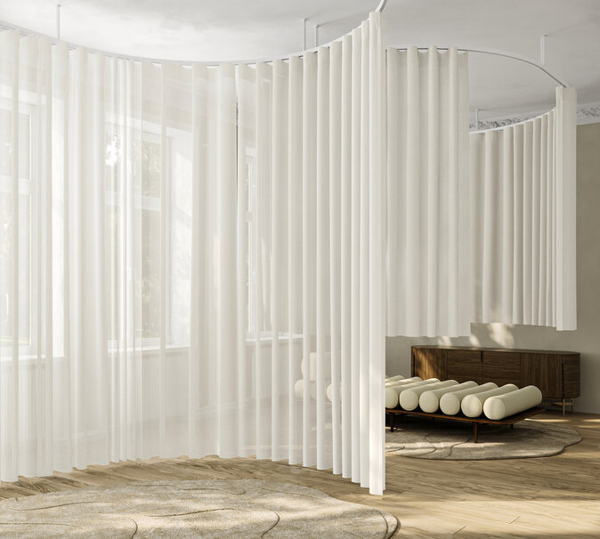 Jasny salon z okrągłą sofą i białymi, półprzezroczystymi zasłonami dzielącymi przestrzeń.