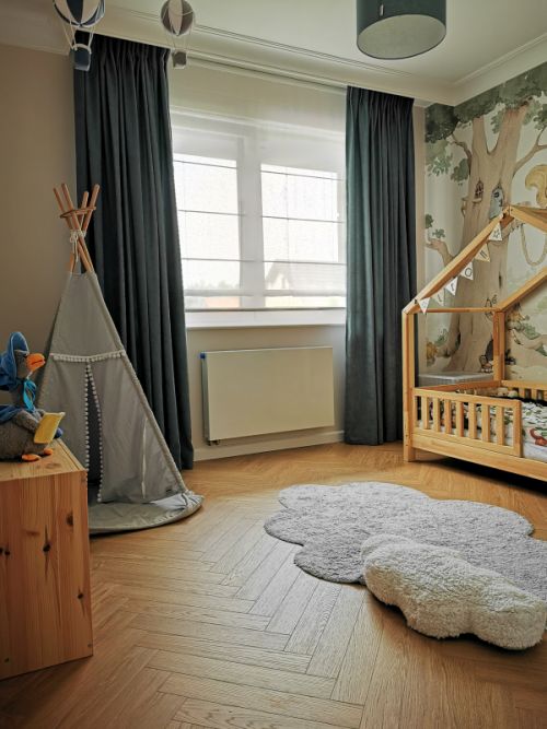 Pokój dziecięcy z tipi, łóżkiem domek i dywanem w kształcie chmurki, na tle kolorowej tapety z drzewem.