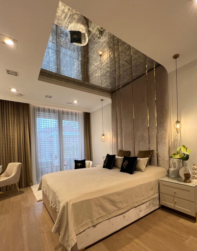 Elegancka sypialnia z dużym łóżkiem, lustrem na suficie i nowoczesnym oświetleniem.